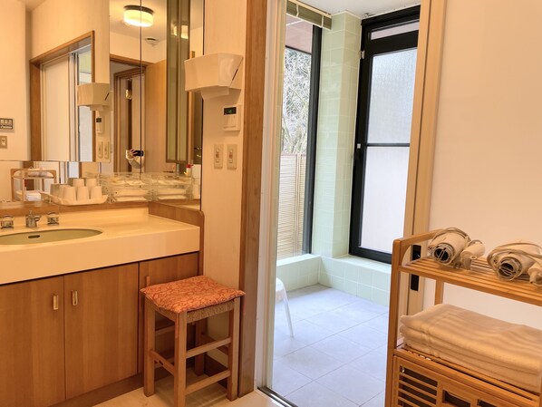 Une salle de bain moderne avec un grand lavabo, un miroir et des meubles en bois. On y trouve un petit tabouret et une étagère avec des serviettes.