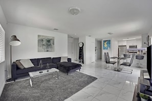 A modern living room with a sofa, coffee table, and a dining area with chairs and a table.