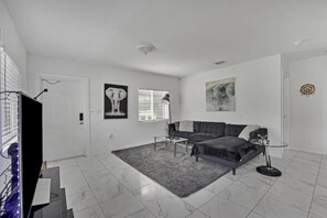 A modern living room with a sofa, a coffee table, and a flat-screen TV. - Close To Airport, Miami & Wynwood New Modern Home! (Miami)