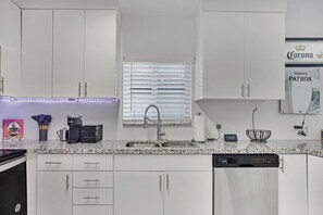 Une cuisine moderne avec des meubles blancs, un plan de travail en granit, une machine à café et une horloge.