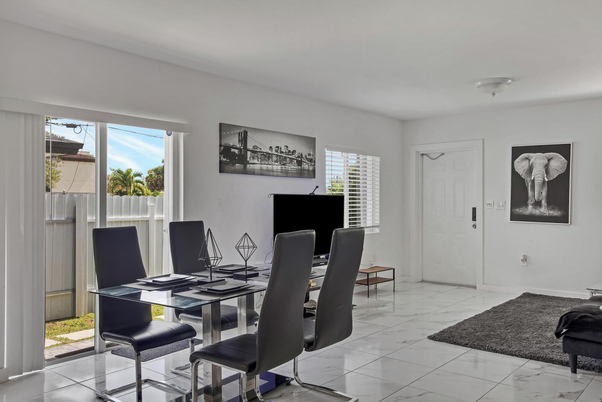 A modern dining area with a glass table, black chairs, and a flat-screen TV.