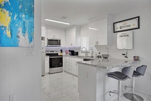 A modern kitchen with white cabinetry, a microwave, a stove, and a bar area with two stools. - Close To Airport, Miami & Wynwood New Modern Home! (Miami)