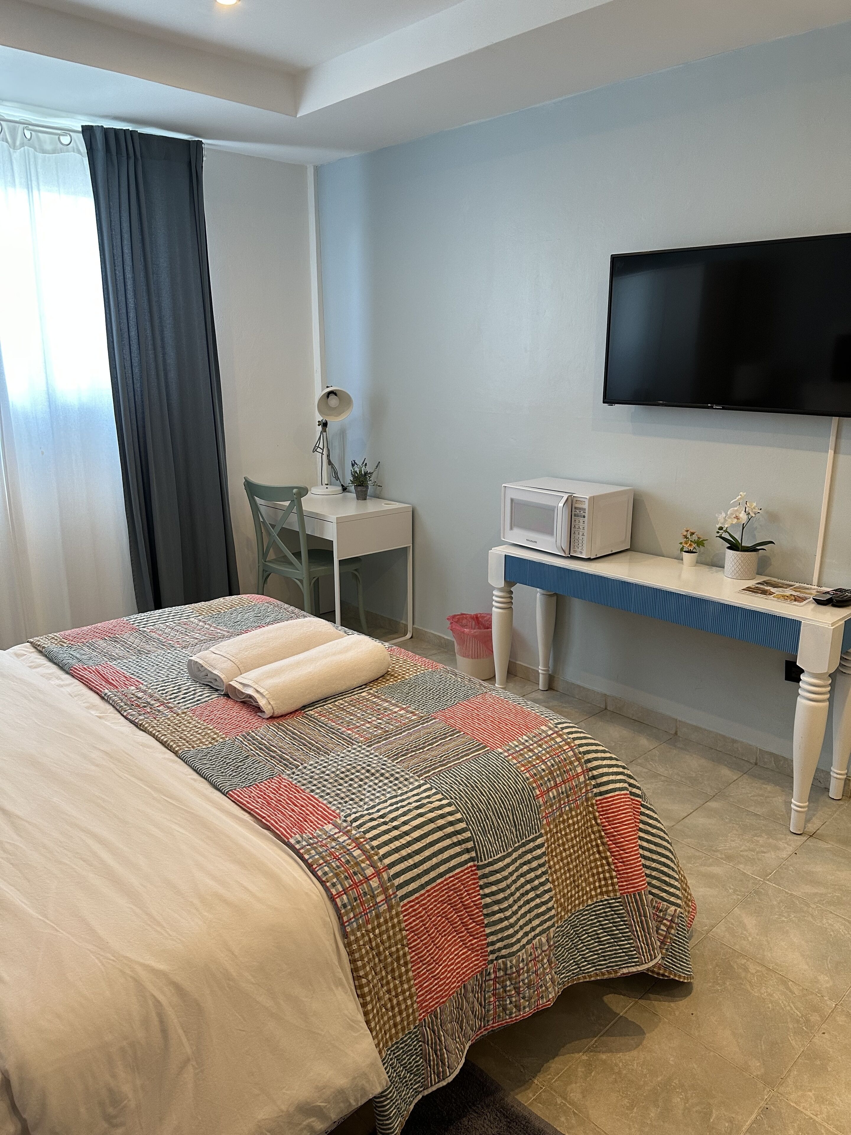 A hotel room with a bed, a desk, a television, and a window with curtains.