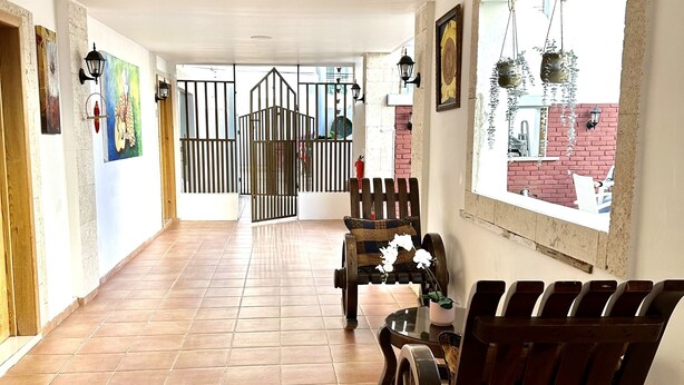 A corridor with tiled flooring, a bench, a table with a vase, and a view through a window.