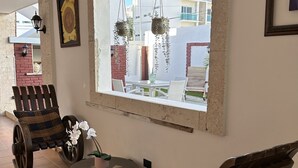 A cozy seating area with rustic wooden chairs and a small table, a large window with a view of buildings, and a hanging plant.