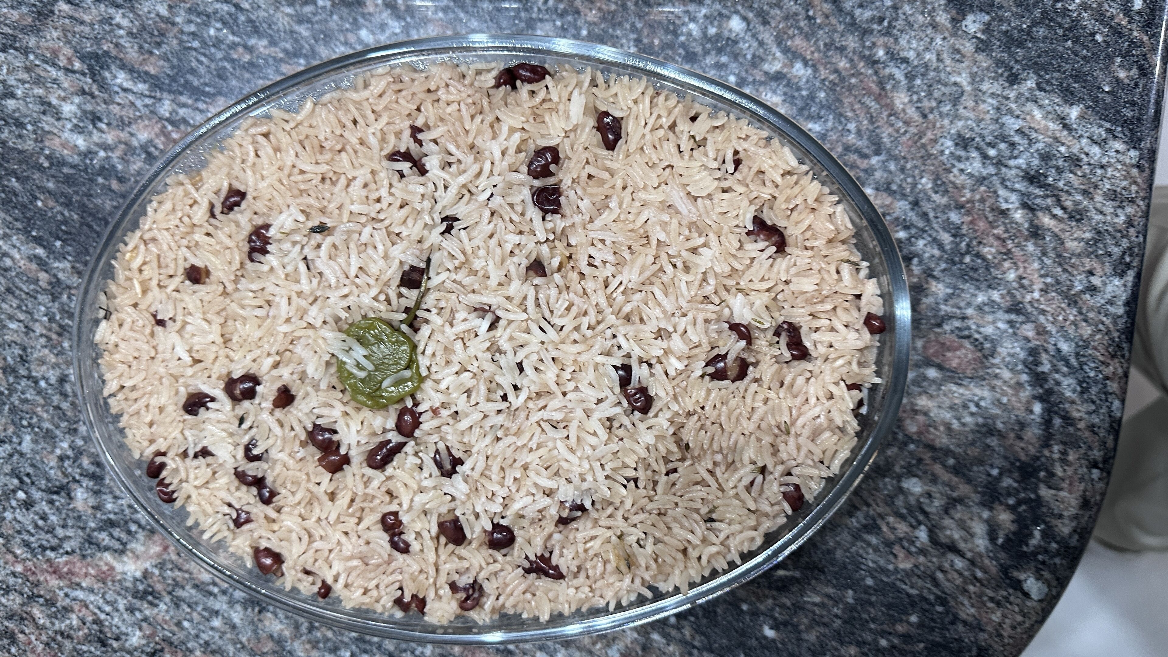 A bowl of rice with raisins and a green pepper on a granite countertop.