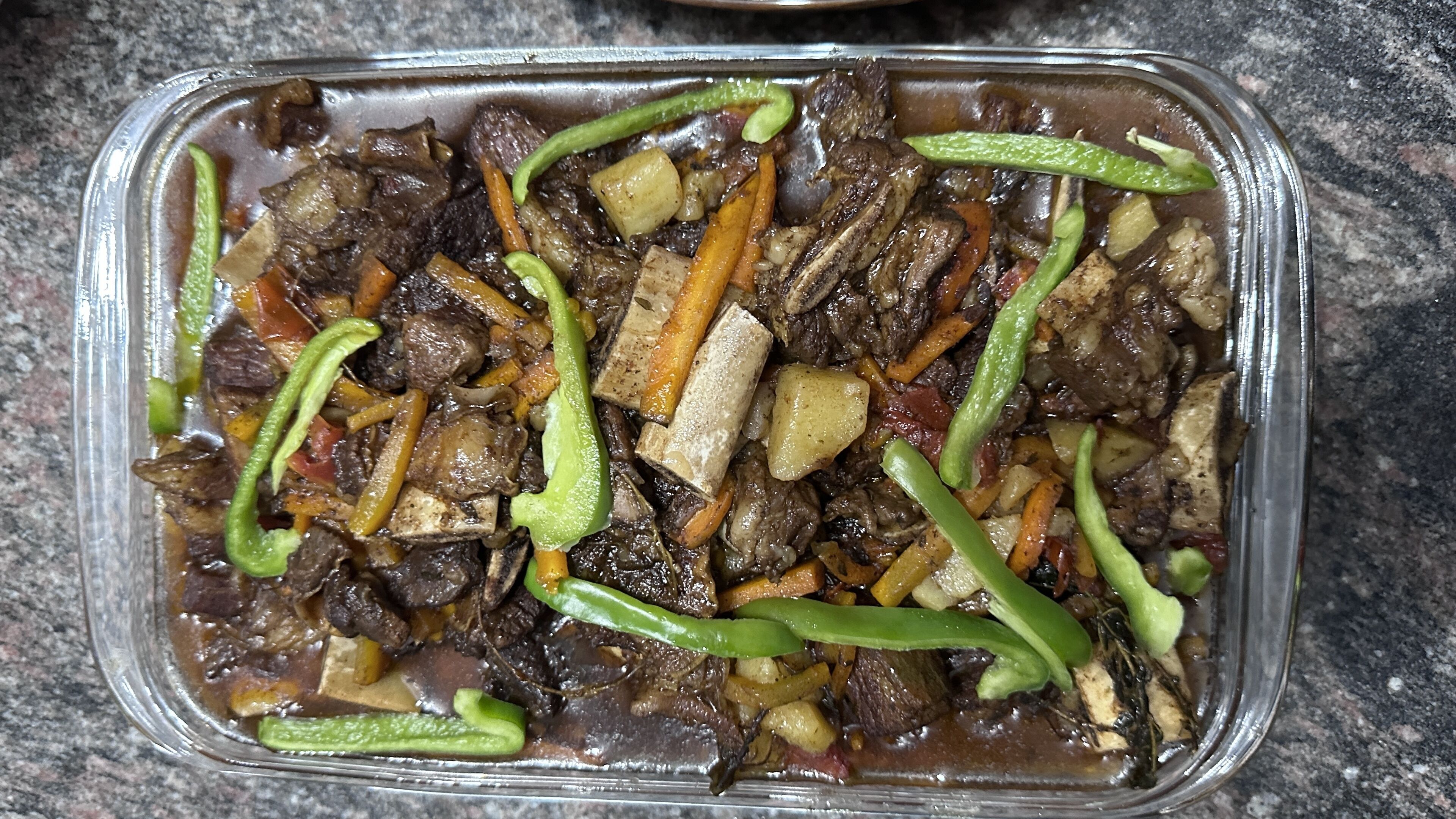 Recipiente de vidrio rectangular con un guiso que contiene trozos de carne, verduras y pimientos verdes.