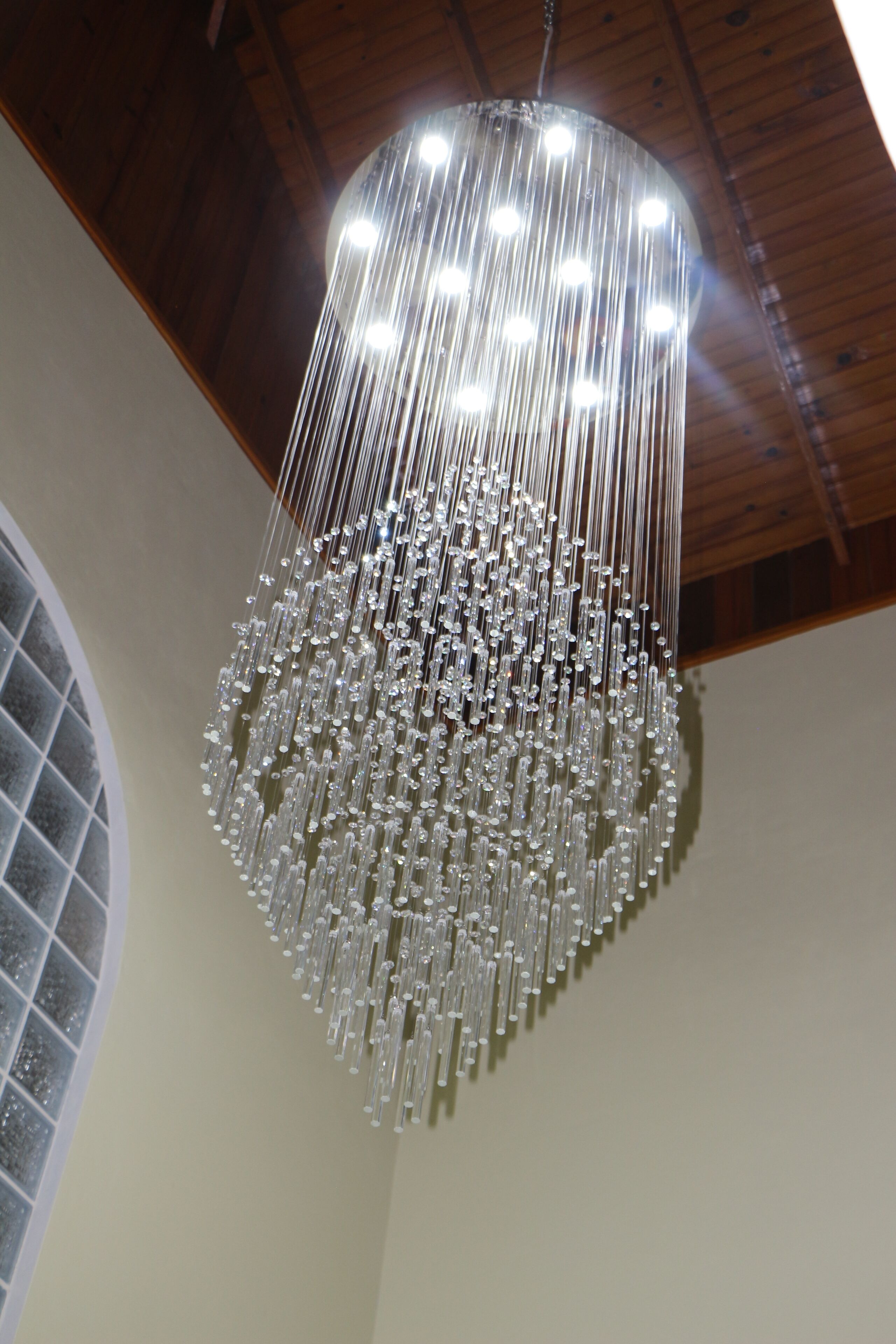 A chandelier with multiple hanging elements in a room with wooden beams and a circular window.