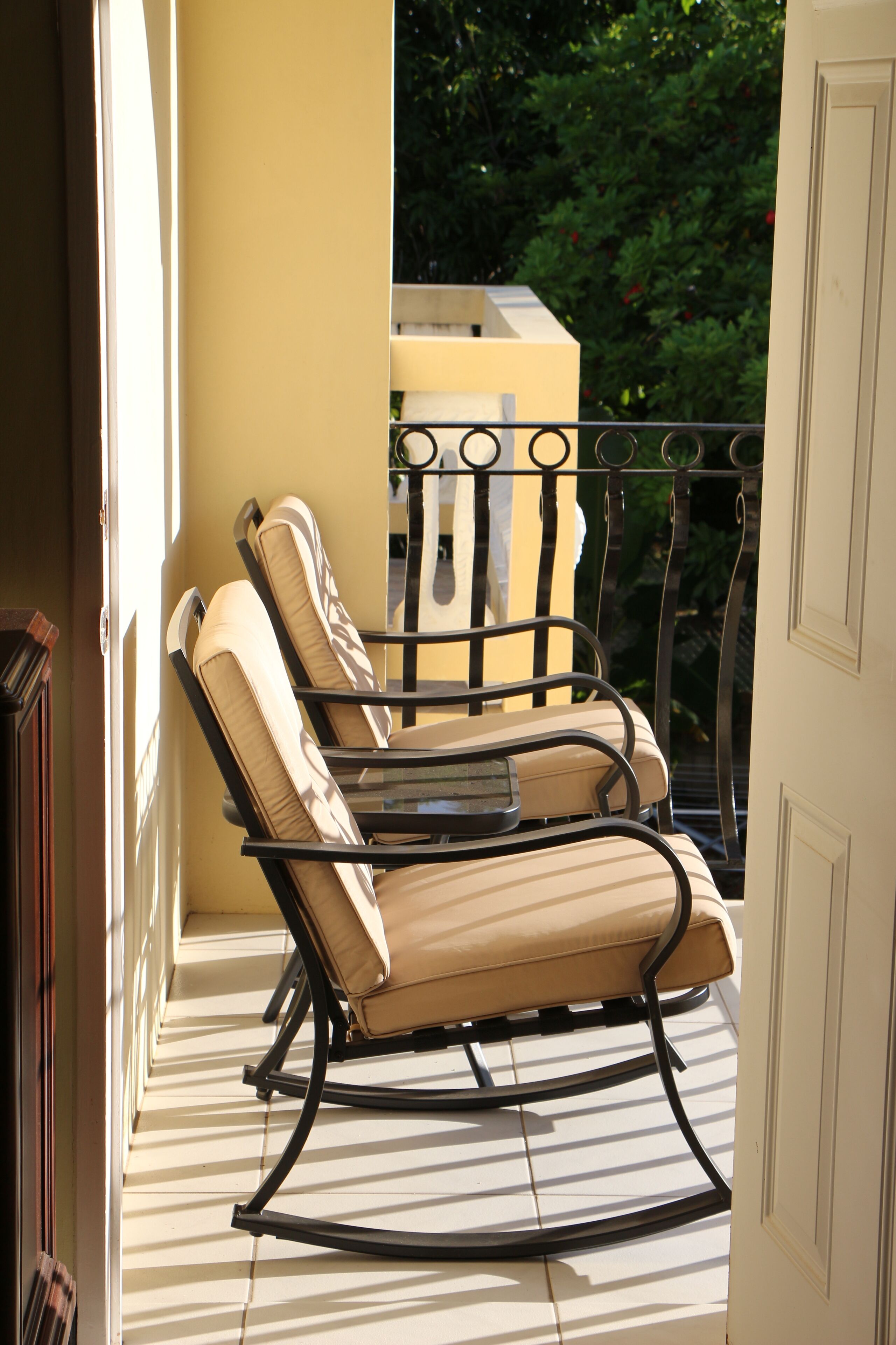A balcony with two rocking chairs and a glass table.