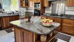 A kitchen with wooden cabinets, granite countertops, a stainless steel range hood, and a microwave. - Villa Nilaja (Montego Bay)