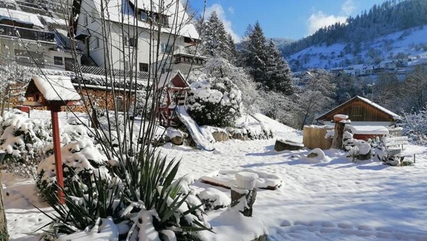 A snow-covered landscape with buildings, a wooden cabin, and a mountain in the background. - Apartment "Am Sersbach" (Forbach)