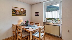 A dining area with a wooden table, chairs, a lamp, and a window with a view of a landscape. - Apartment "Am Sersbach" (Forbach)
