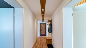 A hallway with wooden flooring, a bench, a door with a patterned design, and a coat rack with hanging items. - Apartment "Am Sersbach" (Forbach)