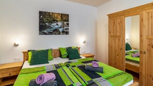 A bedroom with a bed, green and black bedding, a painting of a forest stream, wooden nightstands, and a wardrobe. - Apartment "Am Sersbach" (Forbach)