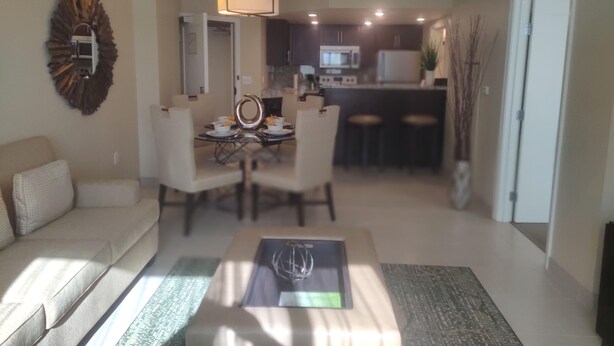 Ein modernes Wohnzimmer mit einer Couch, einem Esstisch und Stühlen. Im Hintergrund ist eine Küchenzeile mit einer Mikrowelle und Schränken zu sehen.