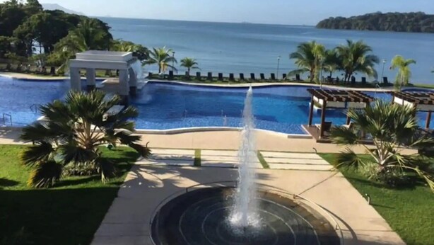 Une piscine avec une fontaine, entourée de palmiers et offrant une vue sur la mer.