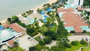 Une vue aérienne d’un complexe hôtelier doté d’une plage, de plusieurs piscines et d’une tour imposante.