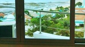 Une vue depuis une fenêtre donnant sur une plage, avec un bâtiment en arrière-plan.