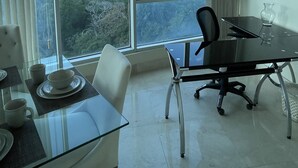Un espace repas moderne avec une table en verre, des chaises blanches et une vue sur un paysage montagneux grâce à de grandes fenêtres.