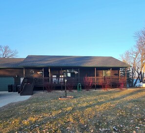A two-story house with a covered porch, a visible garage, and a front yard with grass and fallen leaves. - Rustic house on the lake (Henning)