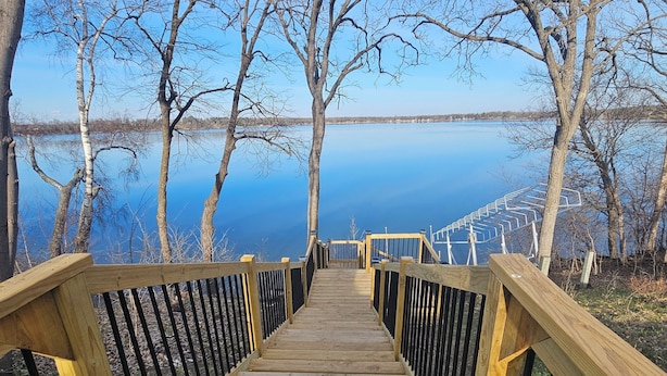 Un escalier en bois mène à une jetée qui surplombe un lac paisible, entouré d’arbres sans feuilles.