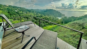 A wooden deck with a table and chairs overlooking a lush landscape and a body of water.