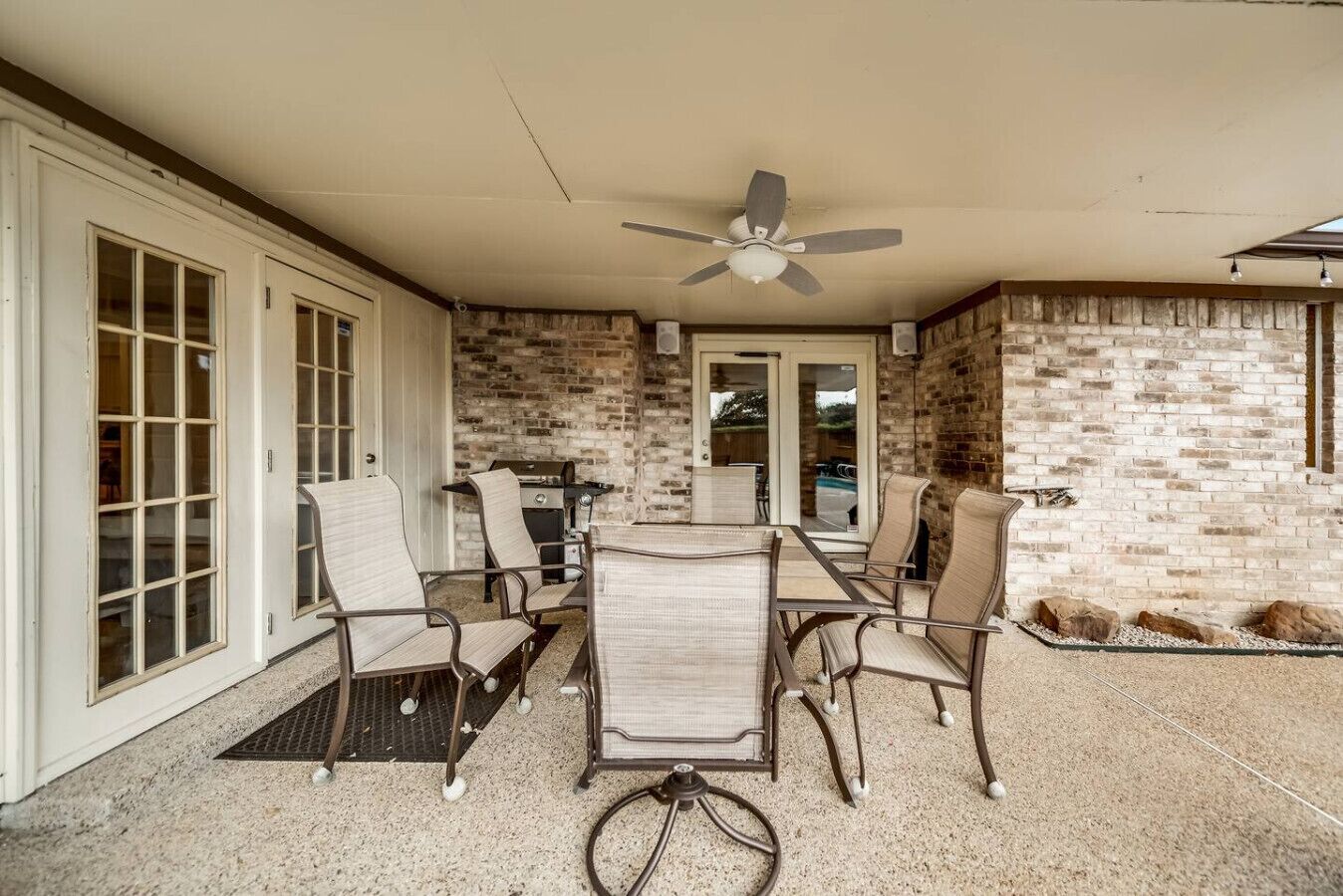 An outdoor patio with a brick wall, a ceiling fan, and a grill.