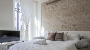 A modern bedroom with a large bed, a flat-screen TV, and a brick-patterned headboard. - Julio Cesar Great Apartment Of High Qualities Heart Of Seville (Sevilla)