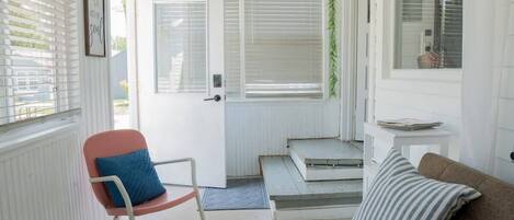 Une pièce avec une porte blanche, un fauteuil à bascule avec un coussin bleu, un canapé marron avec un coussin à rayures et une petite table avec des livres.