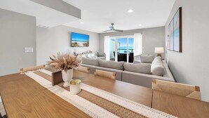 A modern living room with a wooden dining table, grey sofa, and a view of the ocean through large windows. - Summerhaven 3 | Beach Front Townhome with Free Chairs through October! | New Coastal Design! | Tail-Wagging Approved (Miramar Beach)