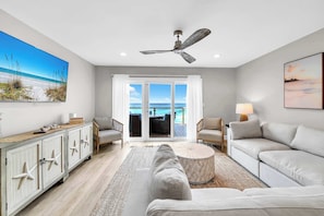 Un salon moderne avec vue sur l’océan, doté d’un ventilateur de plafond, d’une table basse ronde et d’un canapé.
