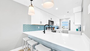 A modern kitchen with white cabinets, a large island with bar stools, and a blue-tiled backsplash. - Summerhaven 3 | Beach Front Townhome with Free Chairs through October! | New Coastal Design! | Tail-Wagging Approved (Miramar Beach)