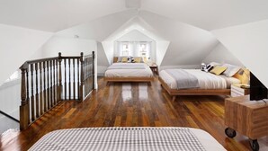 A spacious attic bedroom with a wooden staircase, two beds, and a large window providing natural light.