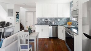A modern kitchen with white cabinets, stainless steel appliances, and a wooden floor.