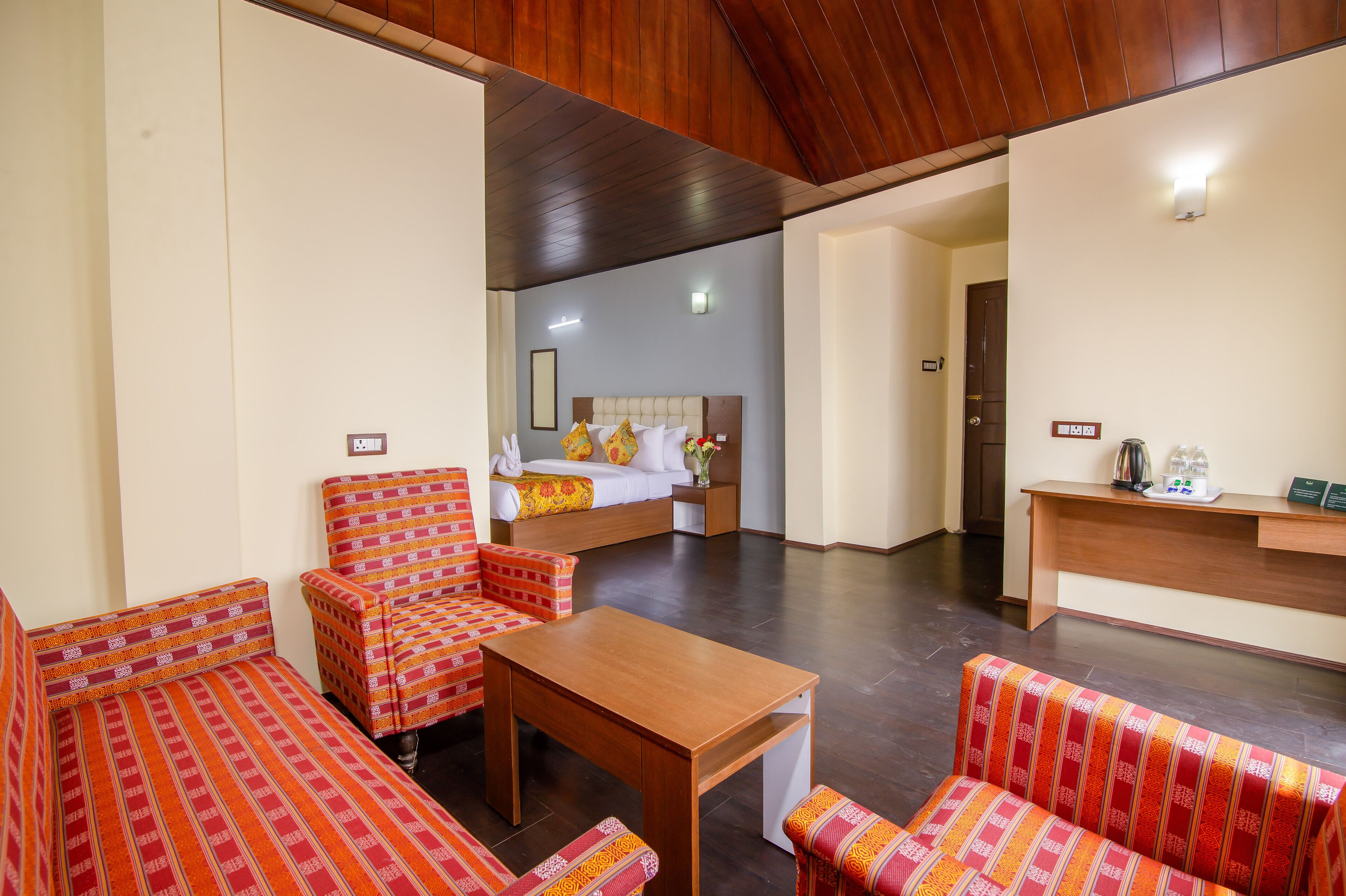 A hotel room with a bed, a wooden desk, and two patterned sofas.