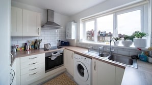 A modern kitchen with a built-in washing machine, a stove, and a large window offering a city view. - Lovely 1Bed Flat - Green Lanes - Spacious and Quiet (Greater London)