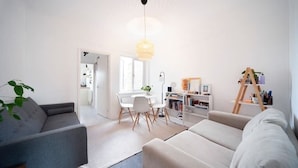 A modern living room with a grey sofa, a beige sofa, a dining area with a white table and chairs, and a bookshelf with various items. - Lovely 1Bed Flat - Green Lanes - Spacious and Quiet (Greater London)