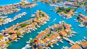 An aerial view of a marina with numerous boats docked, surrounded by colorful buildings with terracotta roofs.
