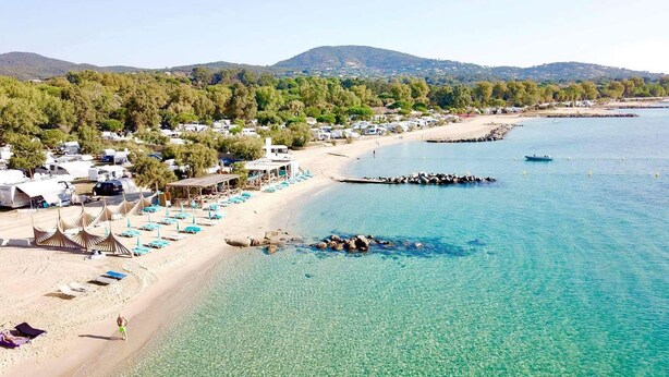 A beach with clear turquoise water, a sandy shore, and a row of beachside tents.