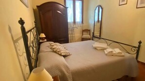 A bedroom with a bed, a nightstand with a lamp, a wooden wardrobe, a mirror, and a window. - Panoramic small house with private pool, situated in the hills above Cortona. Set in a quiet and sec (Cortona)