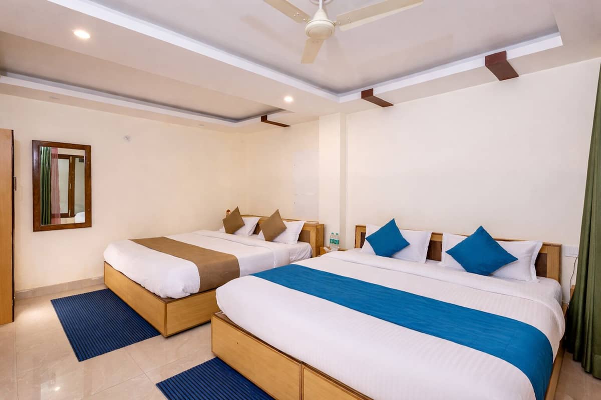 A hotel room with two beds, a ceiling fan, a window with a curtain, and a small table with a bottle.
