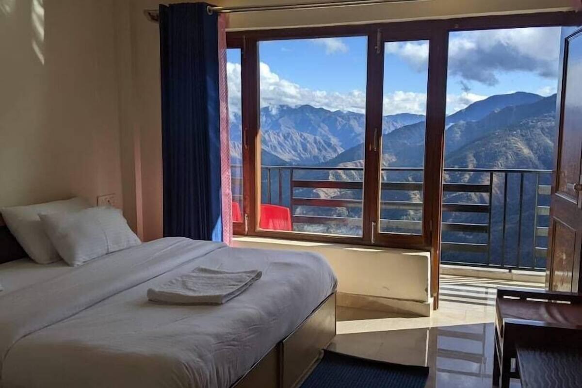 A hotel room with a bed, a window with a mountain view, and a balcony.