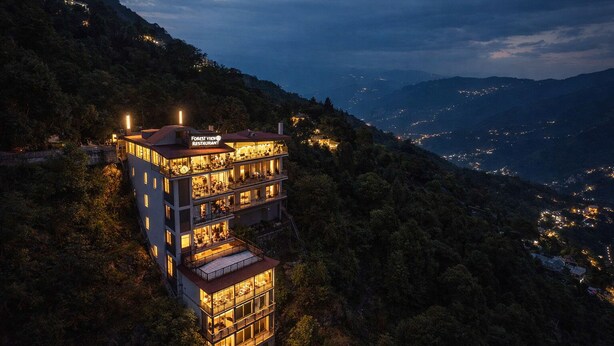 Un immeuble à plusieurs étages doté de balcons, d’une enseigne de restaurant et offrant une vue sur les collines environnantes.