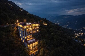 Un edifici de diversos pisos amb balcons, un cartell de restaurant i vistes als turons circumdants.
