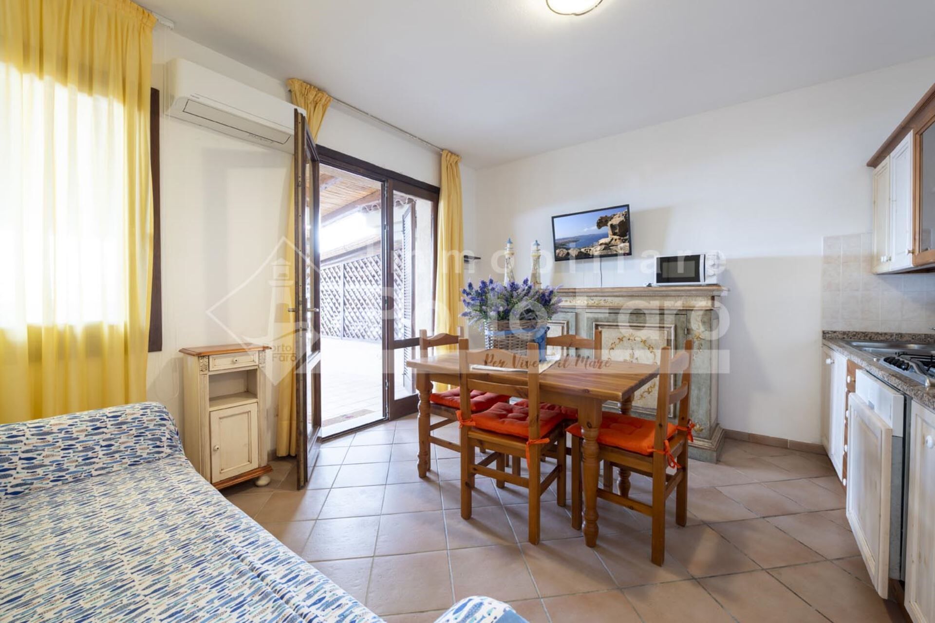 Un espace de vie compact comprenant un lit, une table à manger avec des chaises, un coin cuisine et une porte-fenêtre coulissante donnant sur un espace extérieur.