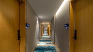 A hotel hallway with wooden doors, a blue carpet, and digital signs indicating room numbers.