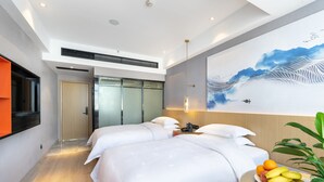 A modern hotel room with two beds, a large artwork on the wall, a fruit bowl on the side table, and a view of the hallway.