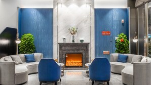 A modern lobby with a fireplace, blue and grey sofas, and a decorative ceiling light.