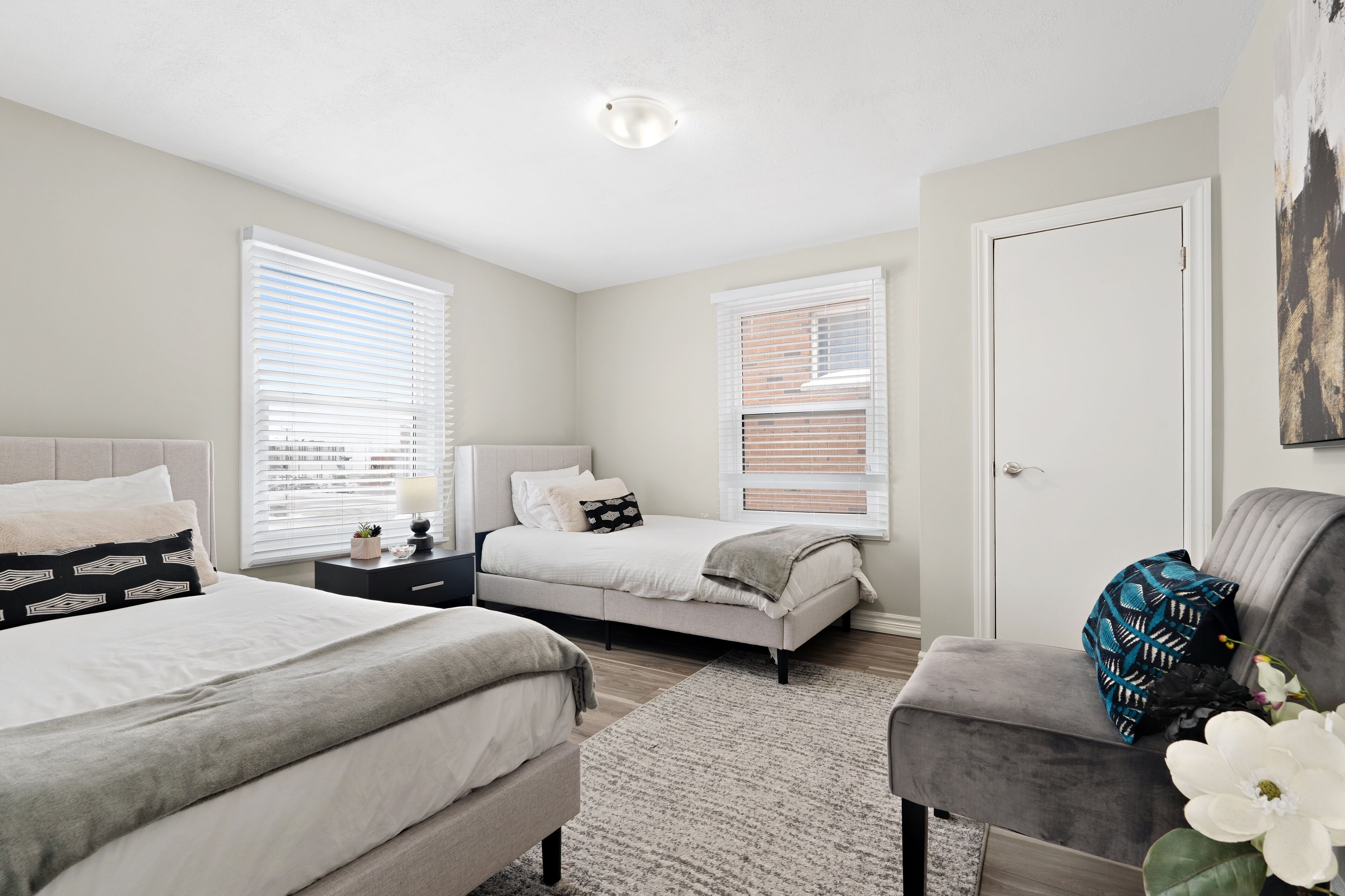 A bedroom with two beds, a nightstand, a dresser, and a gray armchair.
