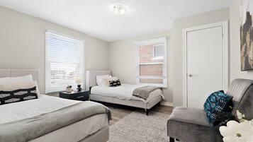 A bedroom with two beds, a nightstand, a dresser, and a gray armchair.